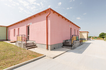 Fototapeta premium Outdoor view of a contemporary educational facility featuring bright colored railings, pink and beige buildings, concrete entrance stairs and a paved walkway under a clear sky.