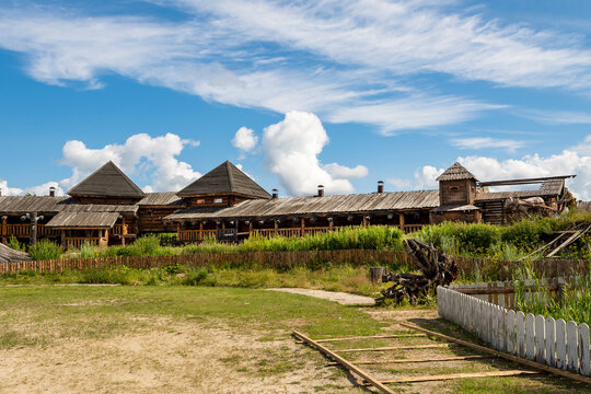 The impressive wooden walls of a reconstructed Old Slavic fortress, made of round, hewn logs. Old barracks and boyar chambers. A bright, sunny day.