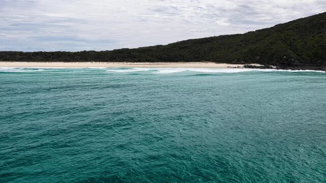 Aerial drone video flying towards Seven Mile Beach following waves as they roll into the shoreline. The forward motion captures ocean movement and natural coastal scenery along the sandy beach.