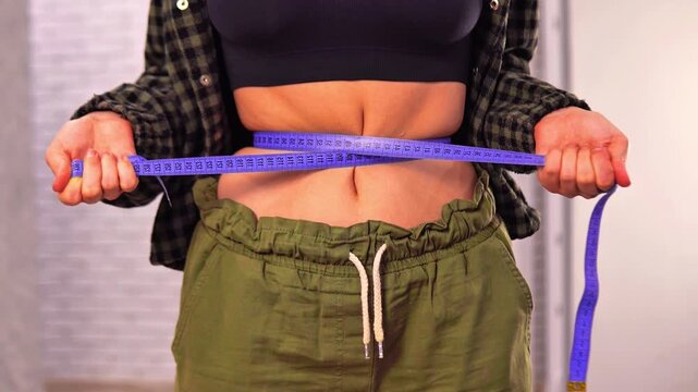 Woman tightly cinching her belly with tape measure