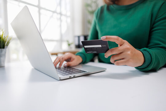 A person is engaged in online shopping, holding a credit card in one hand and typing on a laptop with the other, showcasing modern digital transaction habits.