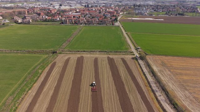 Aerial view of a tractor harrowing agricultural land in Lombardy, Italy, preparing soil for crops in a productive European farming region.