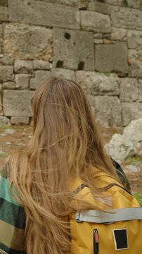 Vertical video. Ancient Greek city of Phaselis, a female tourist with a backpack points to the ruins of an entrance to a house.