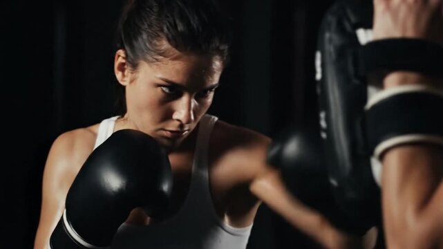 Intense Female Boxer Training and Throwing Punches at Focus Mitts in a Dark Gym Environment