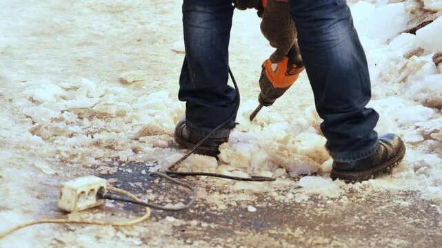 Worker using jackhammer to break ice and frozen ground in winter