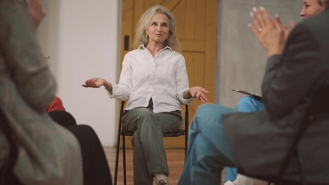 Vertical portrait of pretty aged woman talking about her success in women community. Group therapy with psychologist or informal business meeting, charming grey-haired lady speaking and smiling