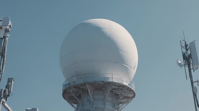 White radome dome housing a radar antenna on a telecommunications tower, collecting crucial weather data and transmitting signals against a clear blue sky