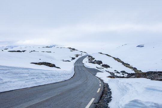 Carretera sinuosa rodeada de nieve con cielo tapado.