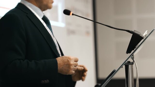 Business speaker giving presentation at conference podium with microphone in modern office or event hall environment.