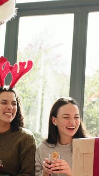 Vertical video: Leaning man in Santa hat causing couch group in living room fistbumping, with gifts