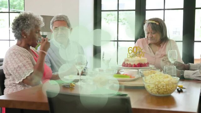 Senior woman giving birthday toast at table, animated '60' sparkles lifting as others raise glasses