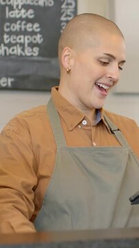 Vertical video: Tapping barista in grey apron using tablet at cafe, taking given phone to pay