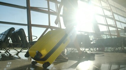Traveler walking through sunlit airport terminal with yellow suitcase, showing themes of arrival, departure, journey, vacation, and modern travel experience © DawDunia