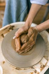 Close up of female hands shaping clay on pottery wheel in ceramic studio, handmade pottery process and traditional craft