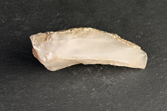 Raw quartz crystal fragment with rough edges on a dark textured background