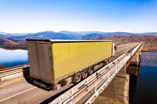 Green truck moving by a bridge over the river