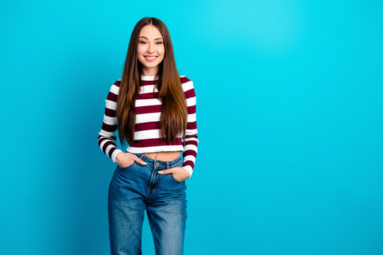 Smiling young woman in striped crop top and jeans standing against bright blue background looking confident and casual