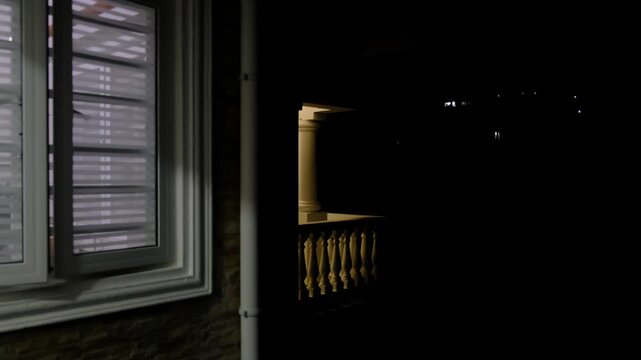 Light inside a house window turns on and off during the night while the surrounding exterior remains dark. The footage shows indoor lighting switching in a residential building, useful for night