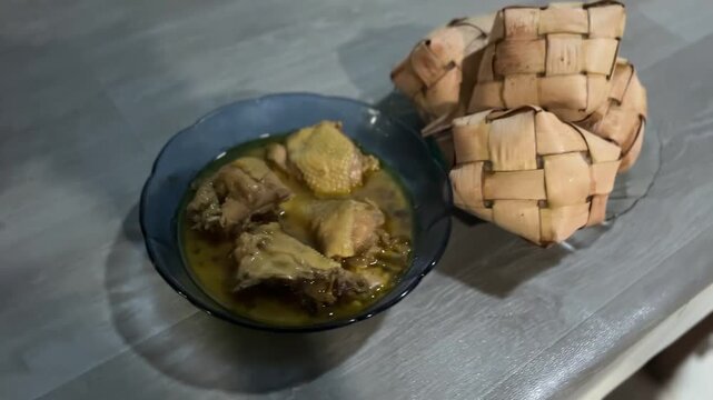 Ketupat rice cakes with chicken curry placed on table indoors during festive mealtime. Shot from top angle, the scene shows traditional food presentation used during celebrations.