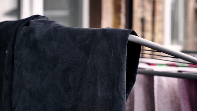 Close-up of black trousers hanging on a laundry rack outdoors with visible lint and detergent stains. Concept of poor washing quality or bad laundry