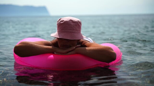 Summer vacation happy woman floats on an inflatable donut mattress, pink swim ring. Summer travel holidays vacation on the sea.