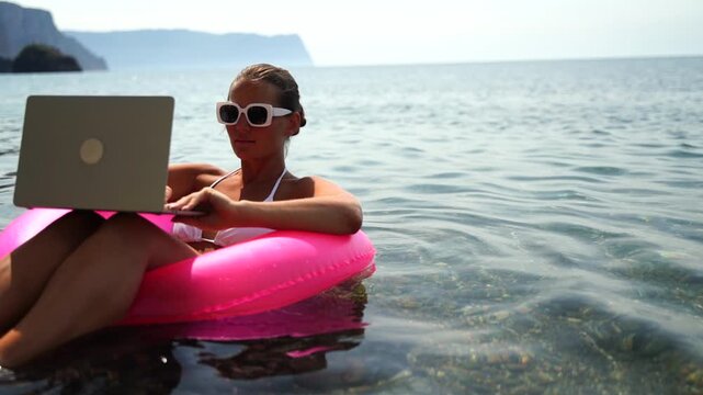 Beach Laptop Woman: Person works on computer floating in sea on sunny day, summer vacation concept.