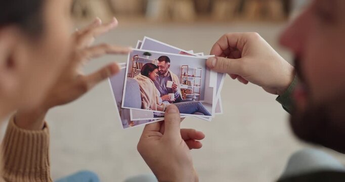 Couple hands holding photos of memories together. Close view of two people sorting prints recalling past moments. Soft focus suggests nostalgia and emotions. Quiet breakup and separation theme.