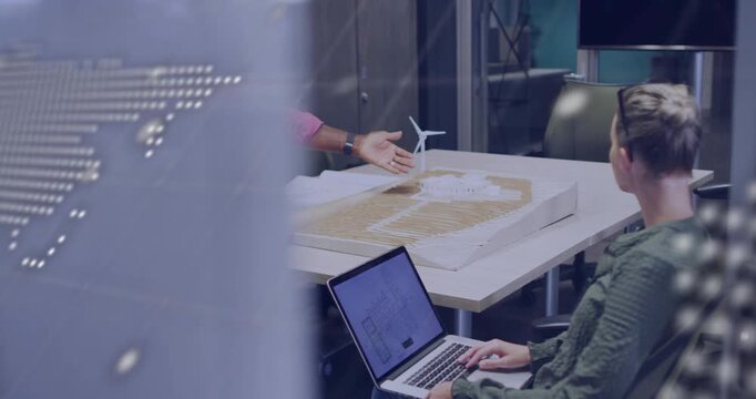 Engineer entering and pointing tablet while colleague typing reviewing turbine with map on glass