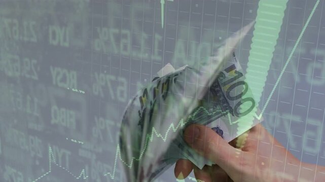 Vertical video: Hand entering frame, fanning 100&euro; bills while stock charts shift, suggesting profit