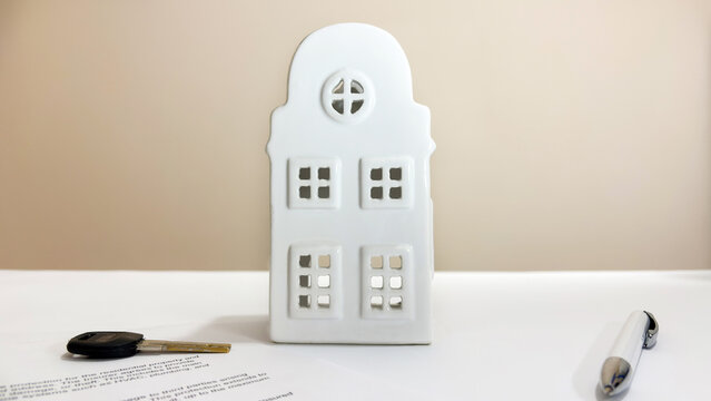 White house model, key and pen lying on a property insurance contract on a light desk, symbolizing mortgage and real estate protection