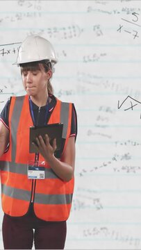 Vertical video: Checking tablet, worker in hi-vis helmet pointing, tapping on math board in studio
