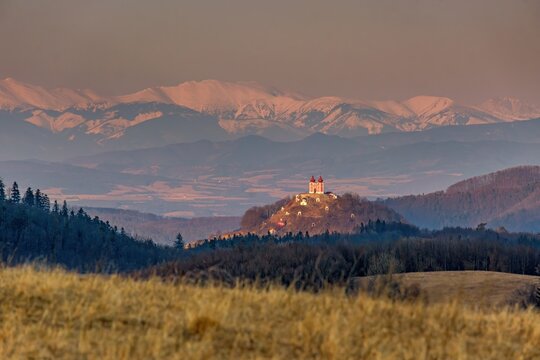 Scenic view of Calvary hill in Banska Stiavnica, Slovakia, with dramatic sunset light and mountain landscape in background. Historic baroque pilgrimage site surrounded by nature.