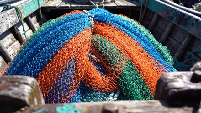 Colorful fishing nets of blue, orange, and green piled inside a weathered wooden boat on a sunny day