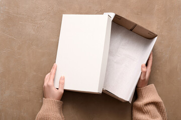 Fototapeta premium Female hands with white open shoebox on brown grunge background