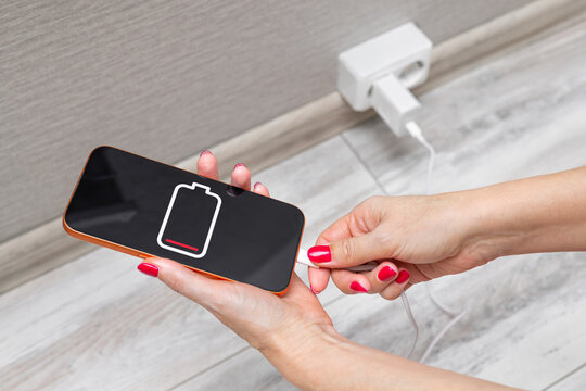 Close-up of a woman's hands charging a smartphone using a cable and USB port. A woman charges a smartphone, close-up. dead smartphone battery. charging your phone at home