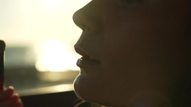 Makeup eyeshadow sunset woman applying cosmetics with a brush during golden hour for an elegant and glowing backlit profile