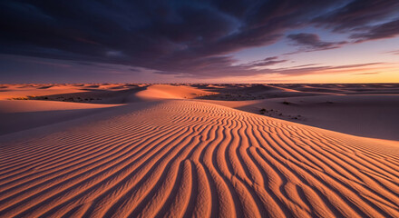 Naklejka premium Vast desert dunes with rippled sand texture under a dramatic sunset sky, symbolizing solitude and natural beauty. Ample free space for text or banner
