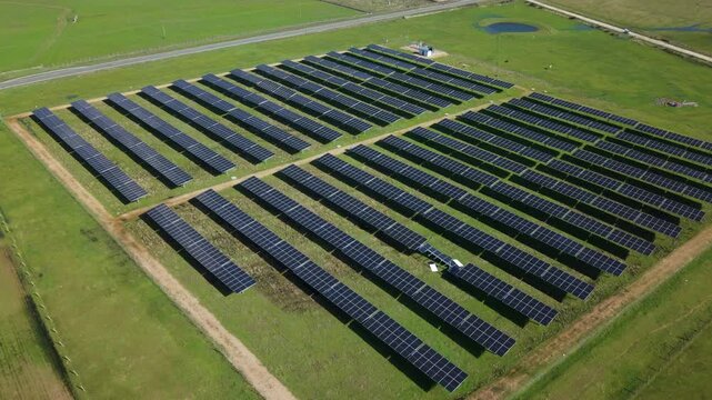 Aerial view of a solar farm generating renewable energy from the sun's rays on a green field in a rural landscape, showcasing sustainable technology and clean power generation