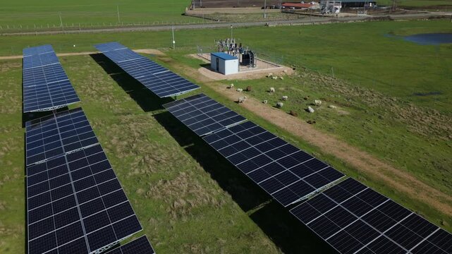 Aerial view of a solar farm with photovoltaic panels generating renewable energy and a herd of sheep grazing in the green field below on a sunny day in Spain