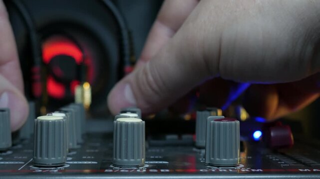 Sound engineer hands adjusting knobs and faders on audio mixer in recording studio.