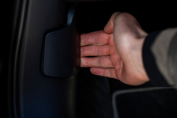 Naklejka premium Driver hand pulling hood release lever under steering column on car dashboard, unlocking engine compartment from inside vehicle interior.