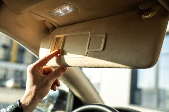 Hand opening cover of vanity mirror in car sun visor, interior detail with overhead light and daylight, automotive cabin close up.