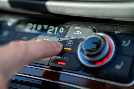 Finger presses rear window defroster button on car climate control panel, activating heating element for rear glass defogging in vehicle interior.