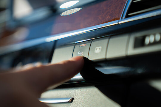 Finger presses parking sensor activation button on car dashboard, enabling parking assist system in vehicle interior.