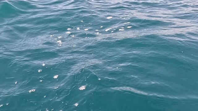 Ocean water ripples gently under sunlight with small splashes in turquoise sea during day