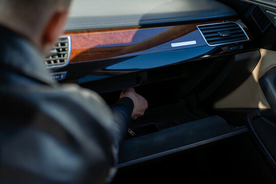 Hand reaching into open glove compartment in car dashboard, interior detail with storage space and trim panel, automotive cabin in daylight.