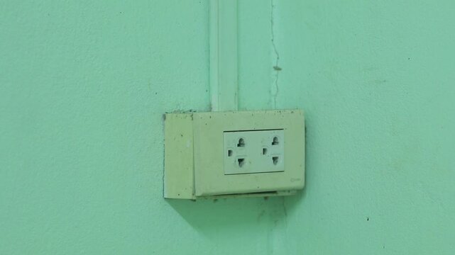 A light blue wall with light switches and electrical outlets for controlling the electricity in the house.