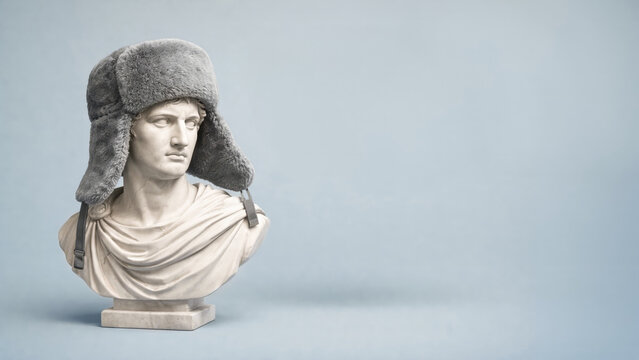 Classical marble bust wearing ushanka hat in studio, humorous cultural contrast, minimal art concept, winter fashion idea, creative sculpture.