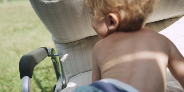 Toddler hiding under a sun lounger cushion on the grass