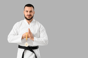 Young man with first place medal practicing karate on light background